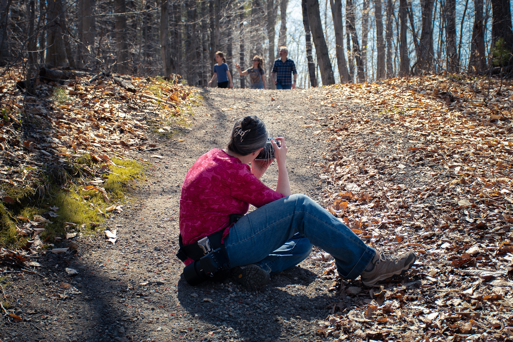 Nadine Tremblay, photographe documentaire, assise sur un sentier forestier pour photographier une famille en balade