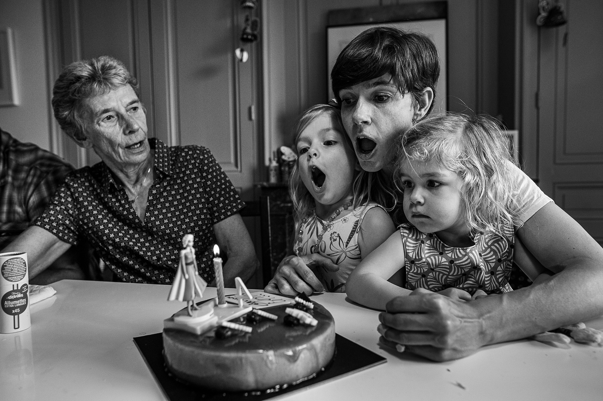 Grand-mère, mère et deux fillettes soufflant ensemble les bougies d'anniversaire, en noir et blanc