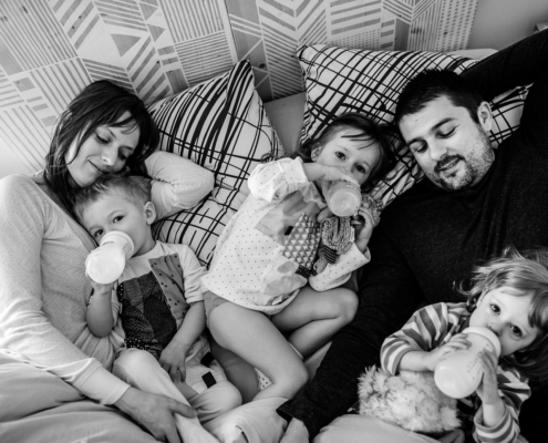 Famille avec trois jeunes enfants buvant leur biberon du matin, allongés dans le lit des parents