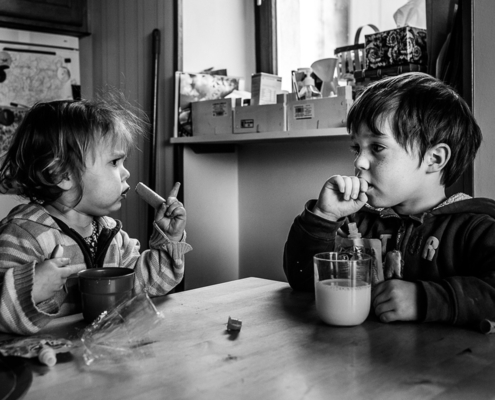 Petite fille et petit garçon assis face à face en train de manger une collation à la table de la cuisine