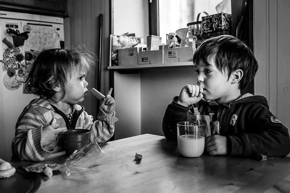 Petite fille et petit garçon assis face à face en train de manger une collation à la table de la cuisine