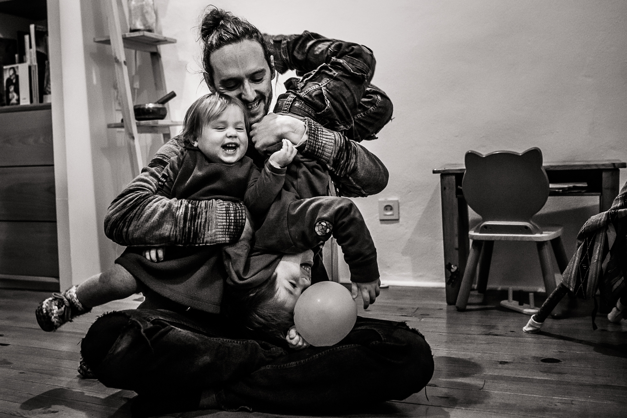 Père au sol qui chahute avec ses deux jeunes enfants dans un éclat de rire