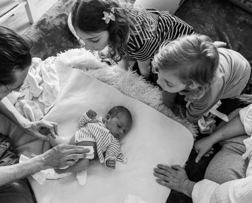 Famille rassemblée autour du nouveau-né allongé sur un coussin, vue plongée en noir et blanc