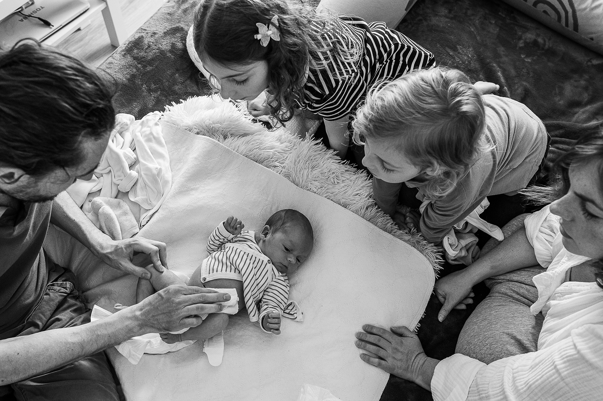 Famille rassemblée autour du nouveau-né allongé sur un coussin, vue plongée en noir et blanc