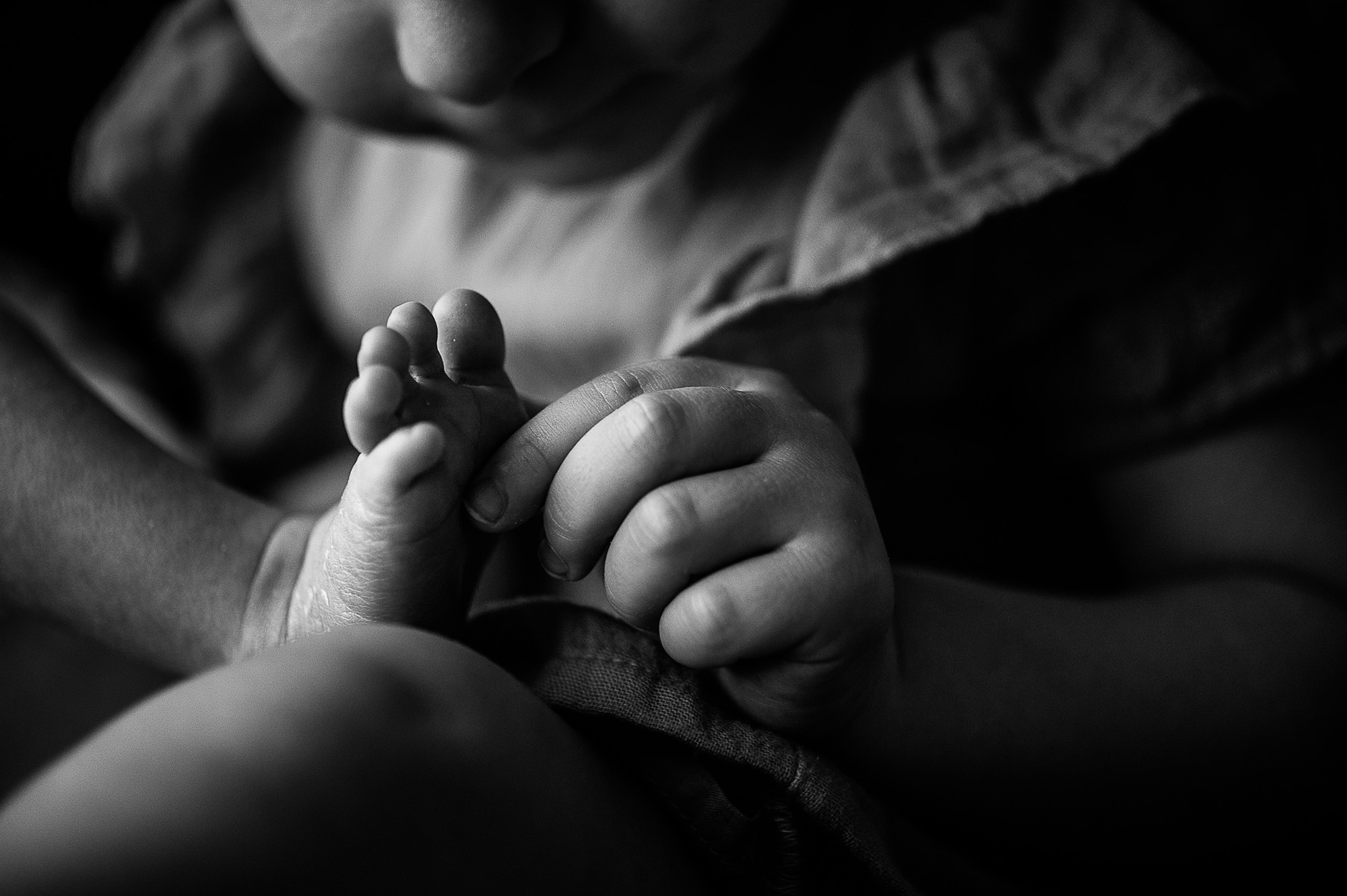Pied minuscule d'un nouveau-né tenu dans la main de sa grande sœur, en gros plan noir et blanc