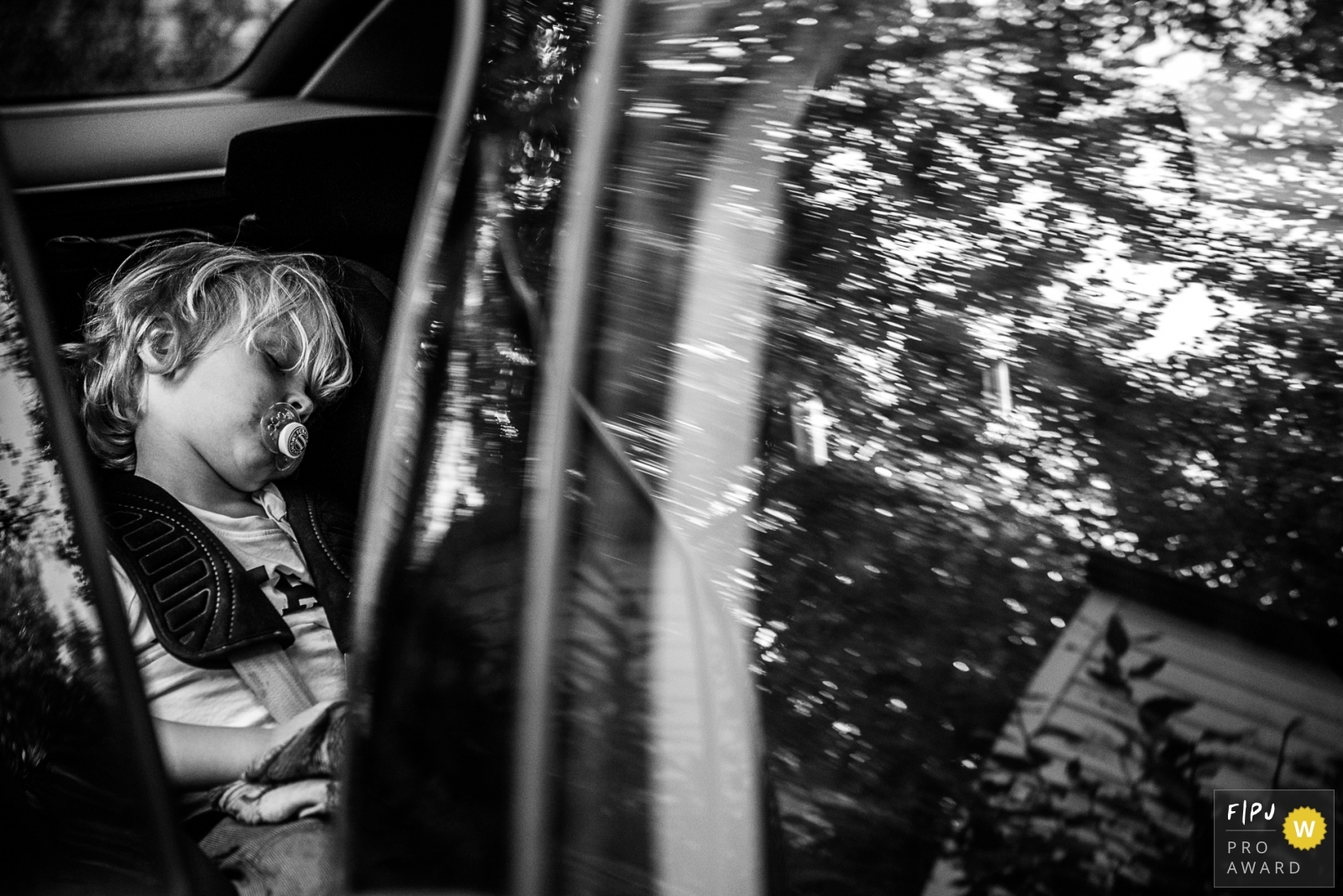 Enfant endormi dans son siège auto avec les reflets des arbres sur la vitre, photo primée Gold Award FPJA